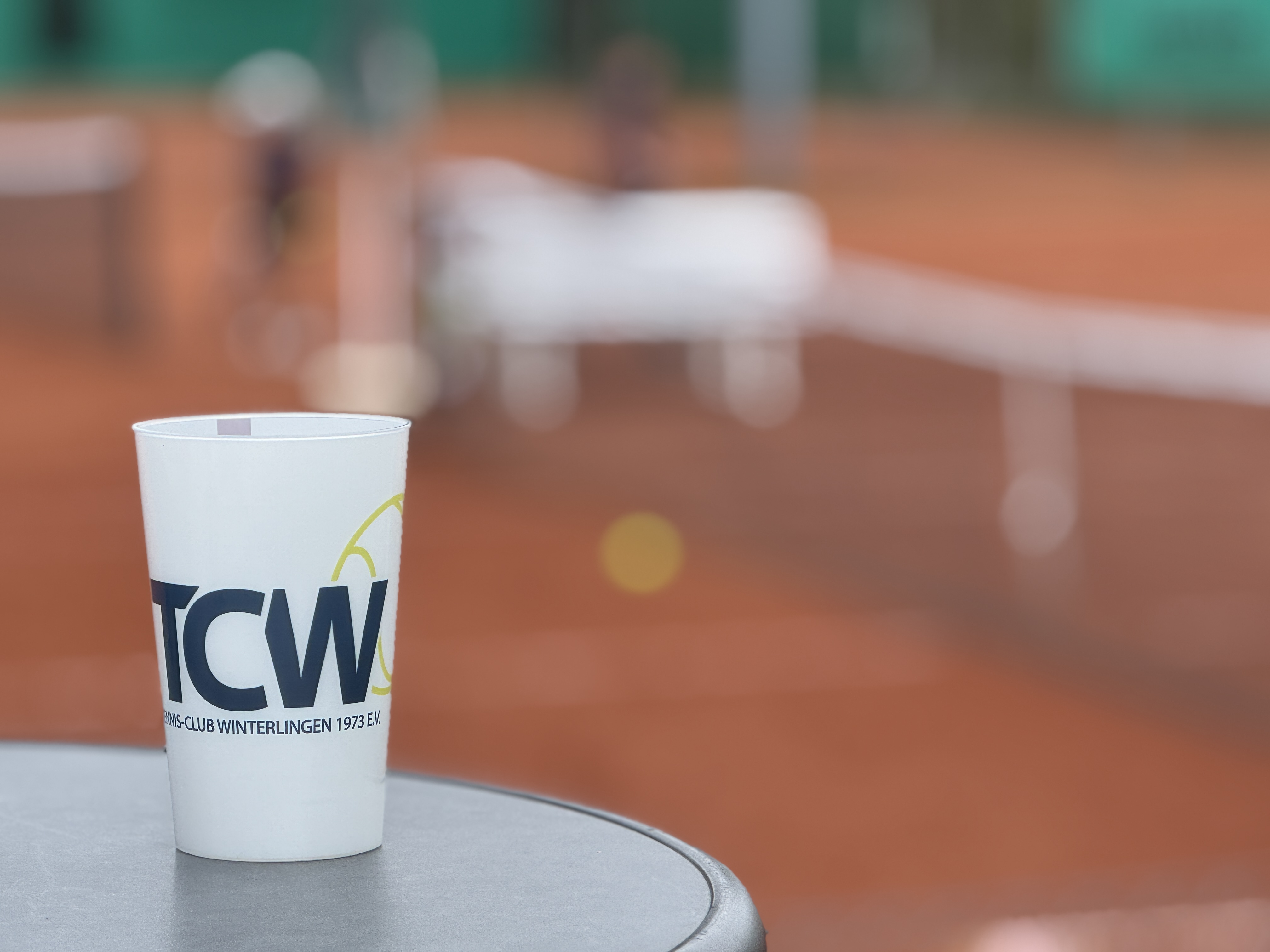 Becher des TC Winterlingen vor einem unscharfen Blick auf die Sandplätze